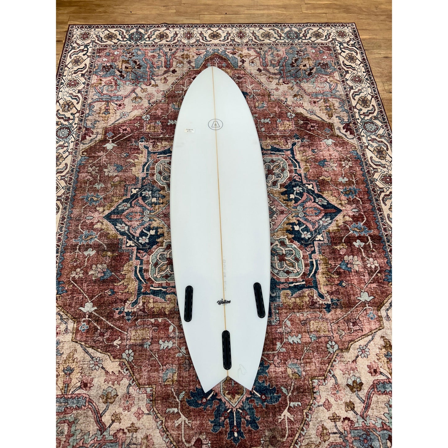 White surfboard with swallow tail on ornate rug, surf equipment at Welcome Boardstore