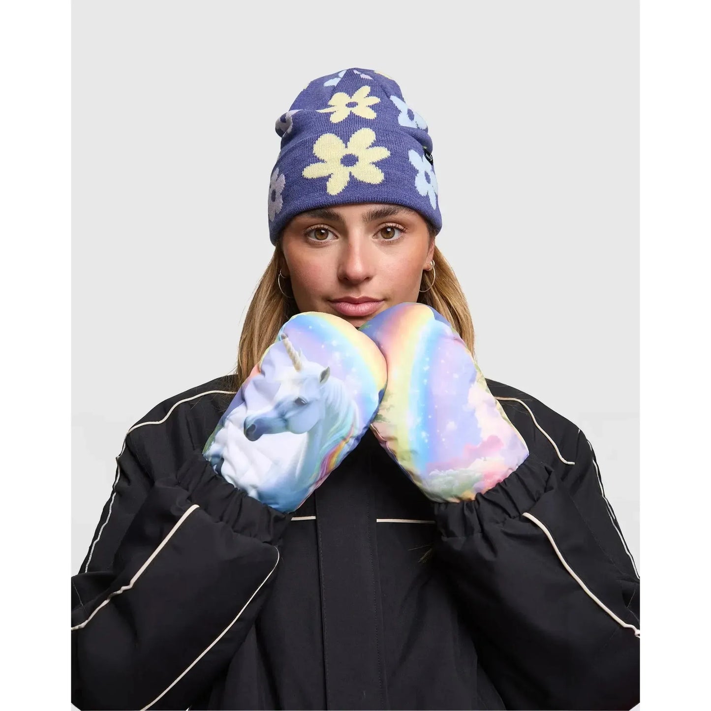 Person wearing a blue floral beanie and colorful mittens with a unicorn design on a plain background