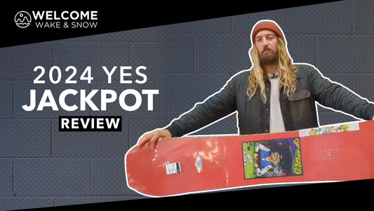 Snowboarder holding red 2024 YES Jackpot snowboard for review at Welcome Boardstore