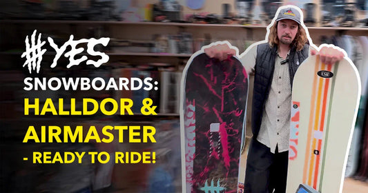 Man in Welcome Boardstore holding YES Halldor and Airmaster snowboards, snowboard shop background.
