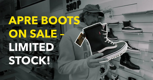 Man holding black apres boots for sale in snowboard shop with boots on display wall