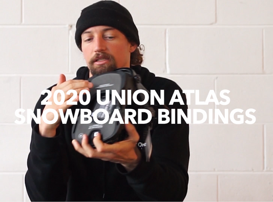 Man in black beanie displaying 2020 Union Atlas snowboard bindings in a shop setting.