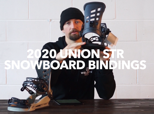 Person showcasing 2020 Union STR snowboard bindings at Welcome Boardstore on wooden table.