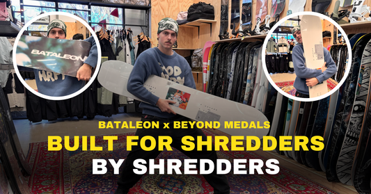 Man in snowboard shop holding Bataleon x Beyond Medals snowboard, surrounded by snowboards.