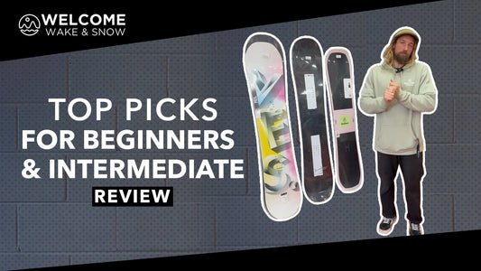 Snowboard expert stands by three snowboards, reviewing beginner and intermediate gear at Welcome Boardstore.