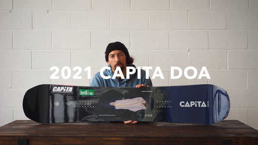 Man holding 2021 Capita DOA snowboard at Boardstore, snowboard equipment review setting