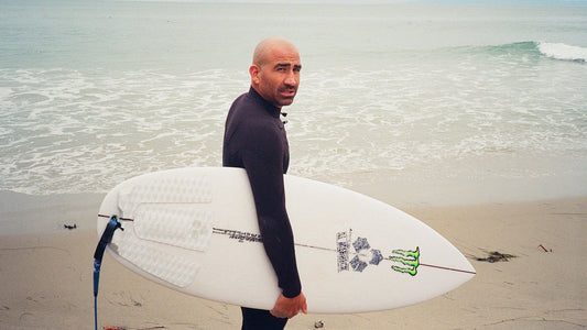 Surfer in a full steamer wetsuit holding a Channel Islands surfboard on the beach
