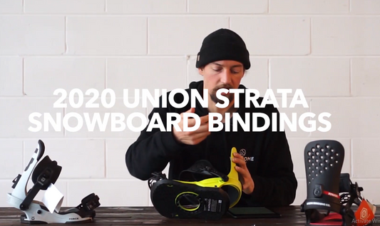 Man in black beanie reviews 2020 Union Strata snowboard bindings on wooden table