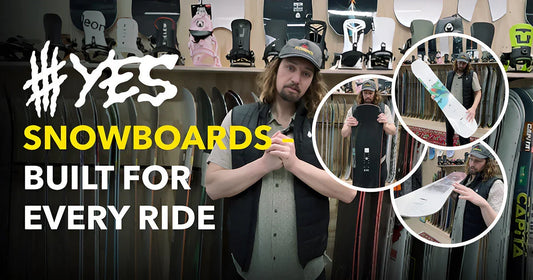Man presenting YES snowboards in board store, surrounded by snowboard gear and equipment display