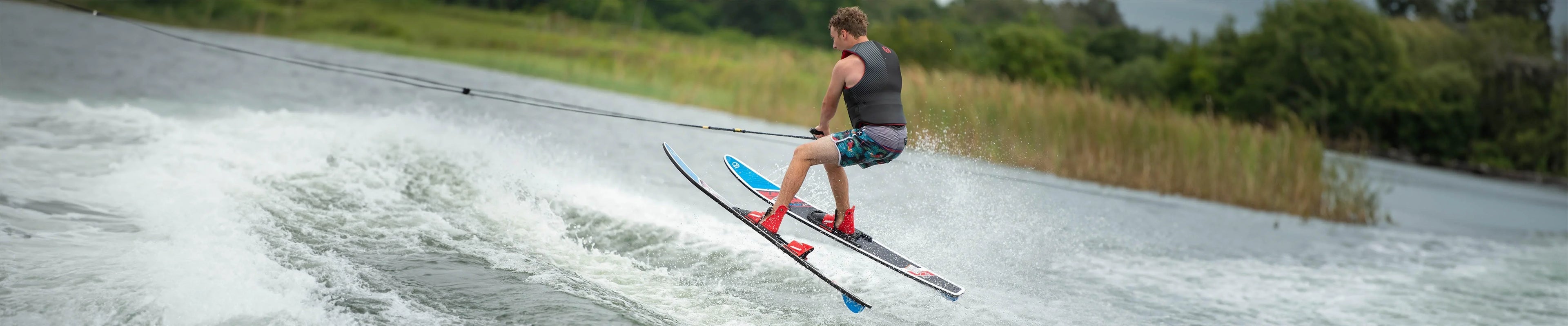 Man water skiing with colorful skis on a lake, wearing a life vest, surrounded by greenery
