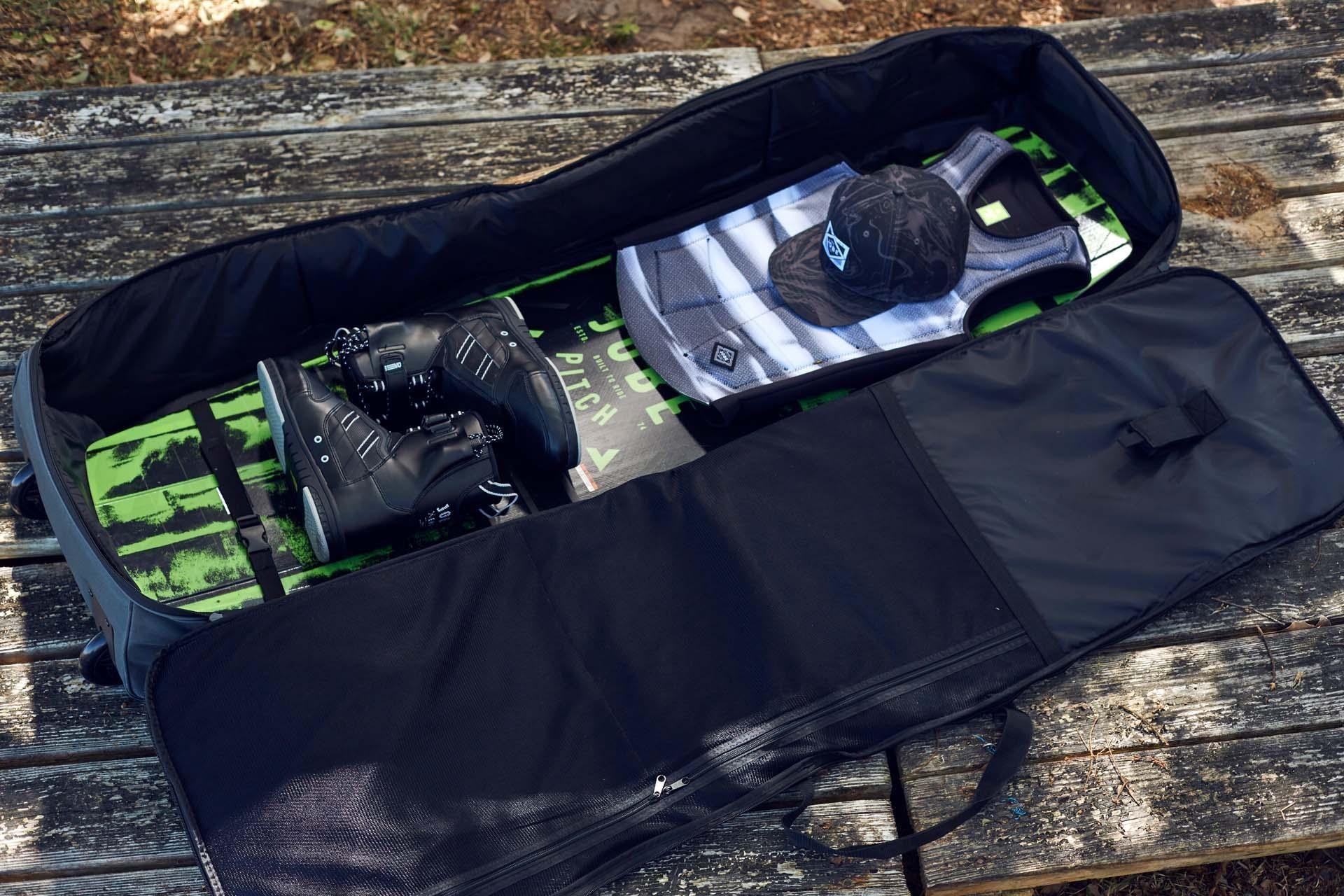 Wakeboard bag with green wakeboard, boots, striped vest, and cap on wooden bench outdoors