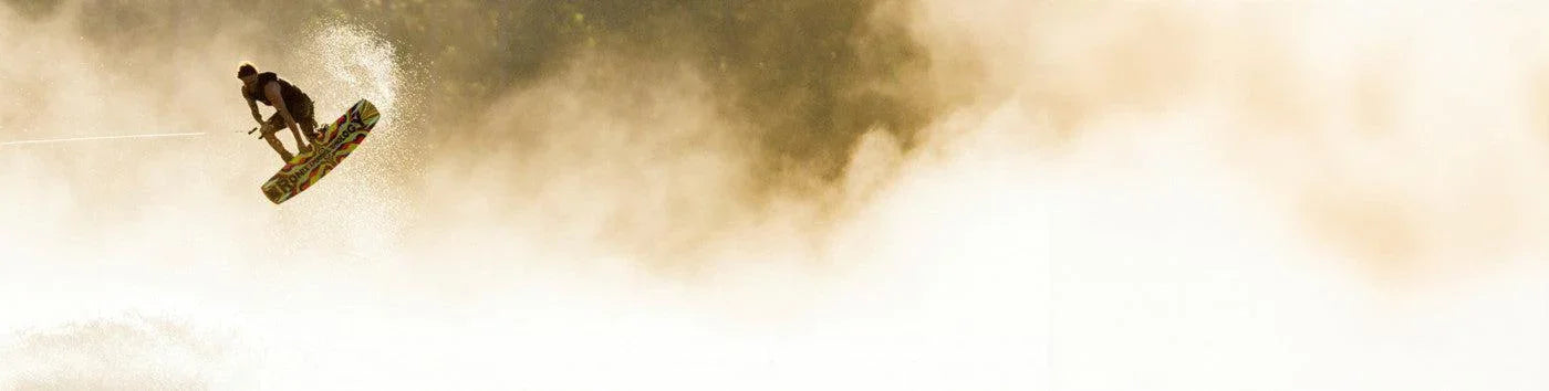 Wakeboarder performing aerial trick over water, spray and sunlight, wakeboarding equipment