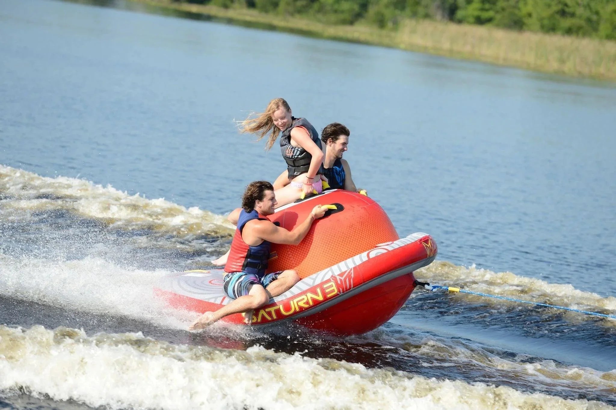 Three people tubing on a lake with safety vests, summer water sport action