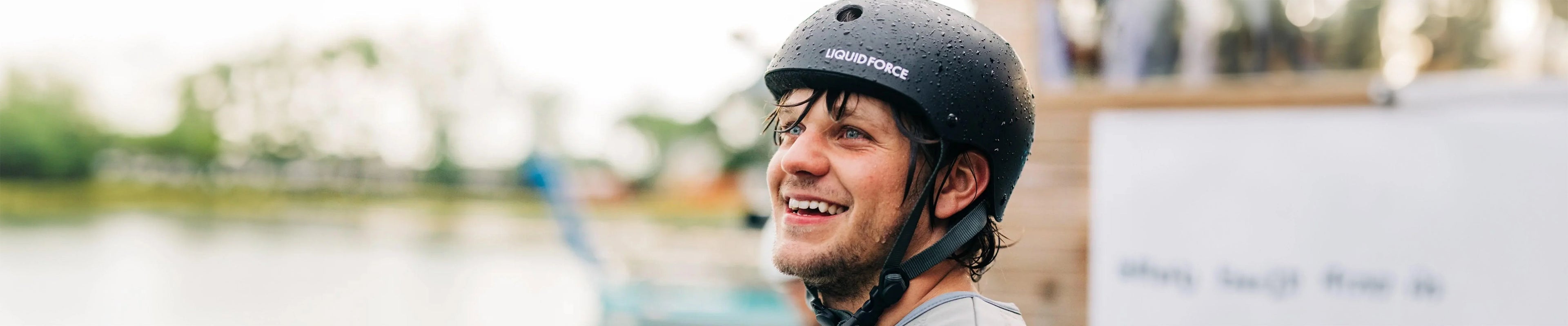 Smiling man wearing a wakeboard helmet by the water at a wakeboarding park