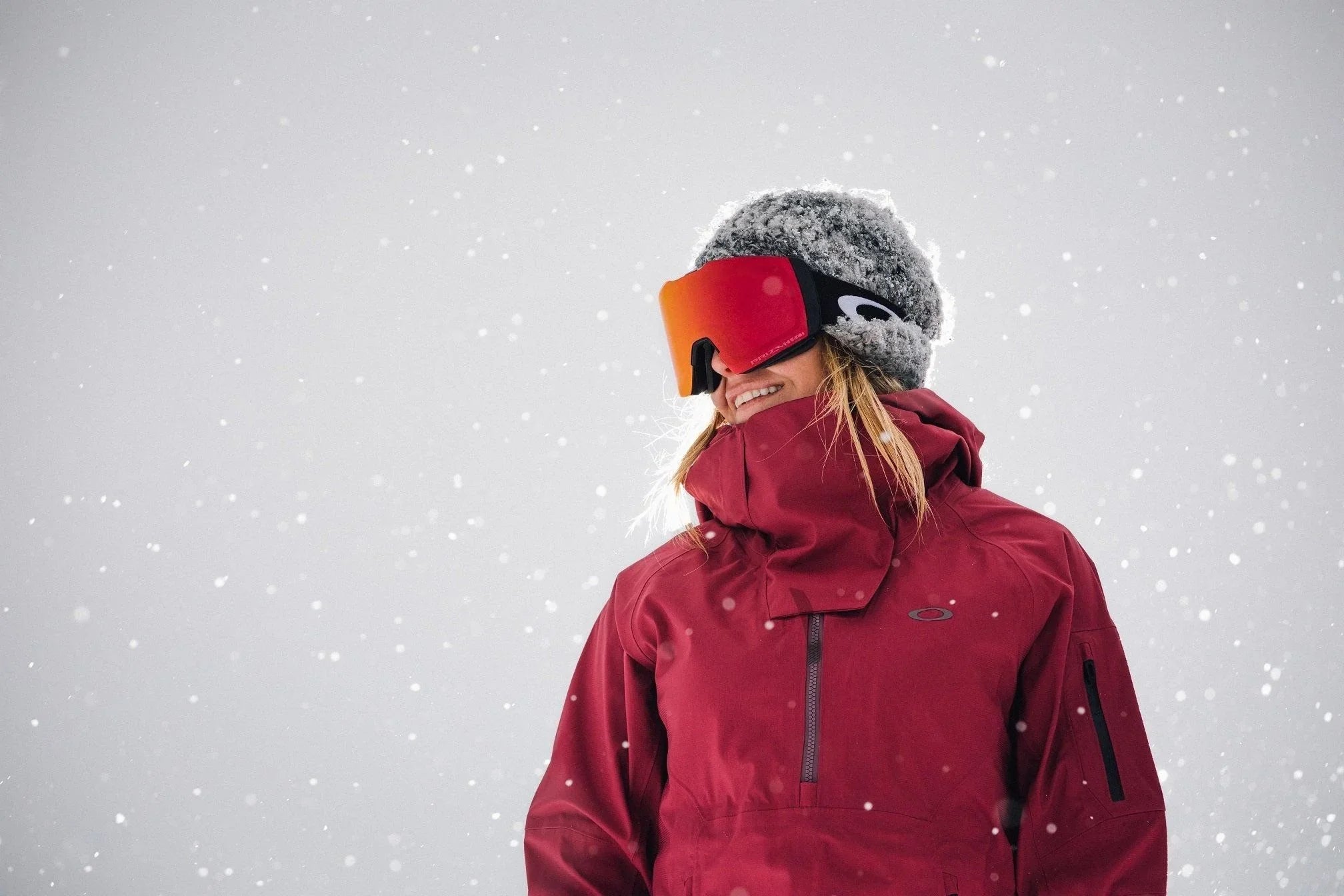 Smiling snowboarder in red jacket and goggles in falling snow, snowboarding gear Australia