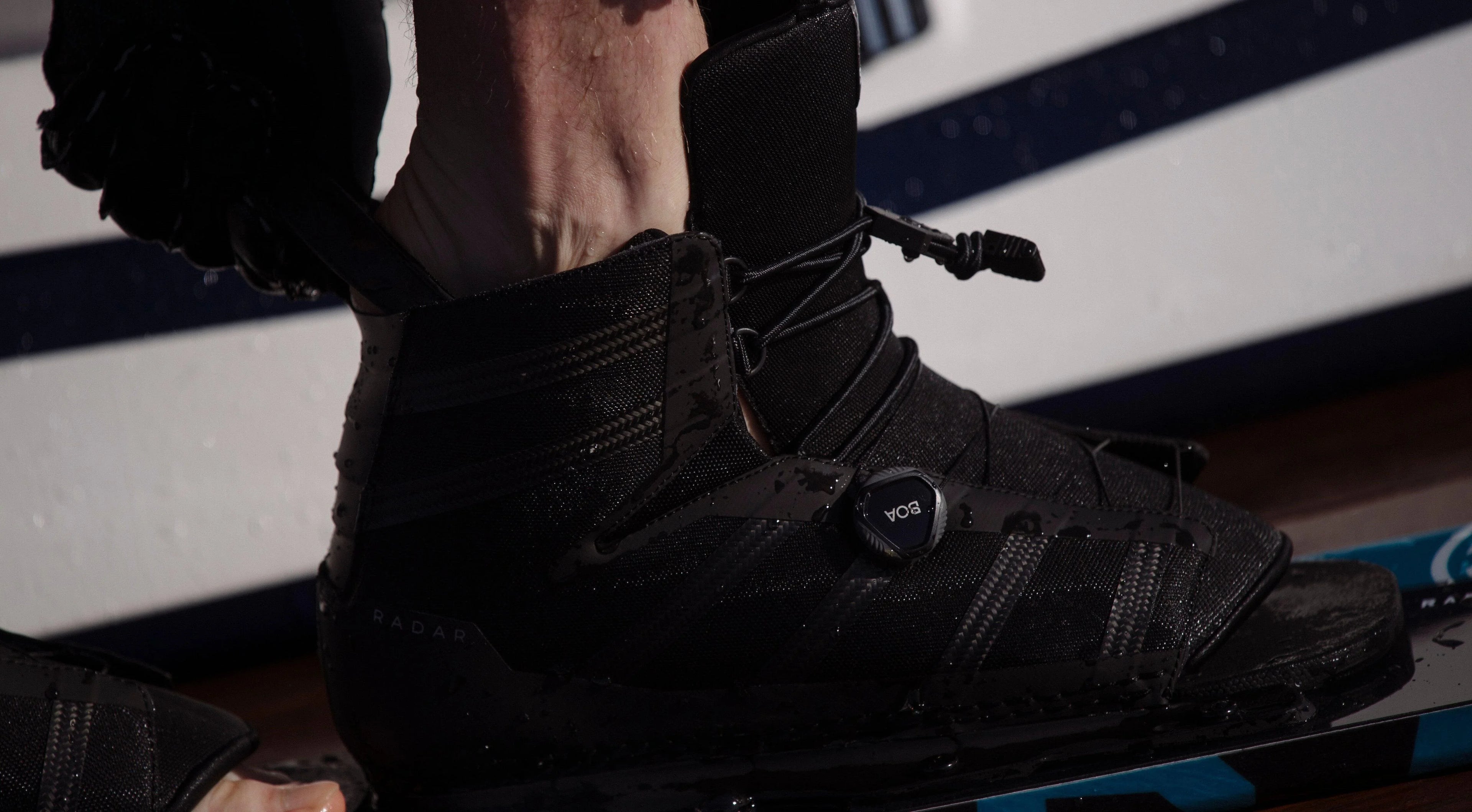 Close-up of a black wakeboard boot with BOA dial on a blue wakeboard, wet and ready for use