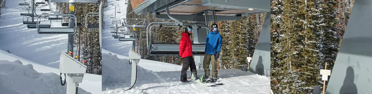 Two snowboarders in winter gear waiting at a snowy ski lift with pine trees in the background