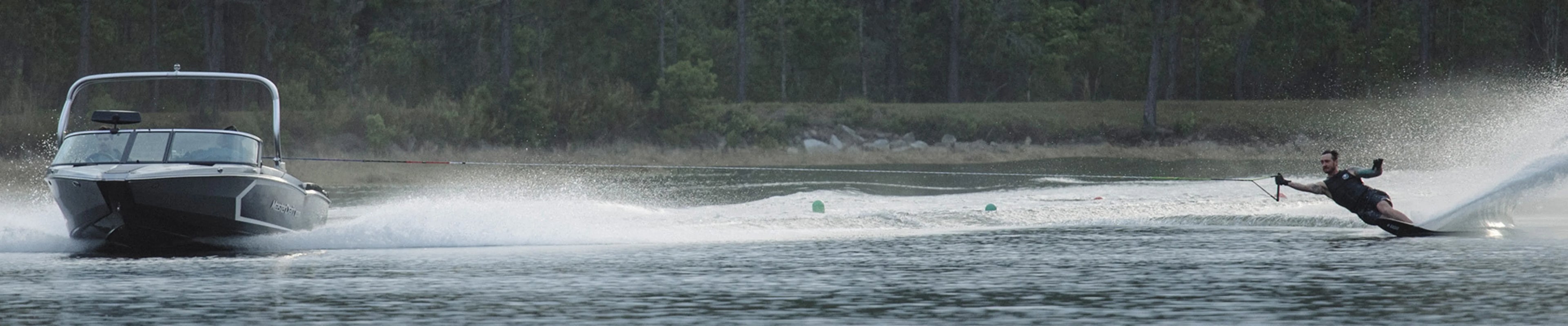 Man wakeboarding behind a speedboat on a lake, surrounded by trees, Boardstore essentials