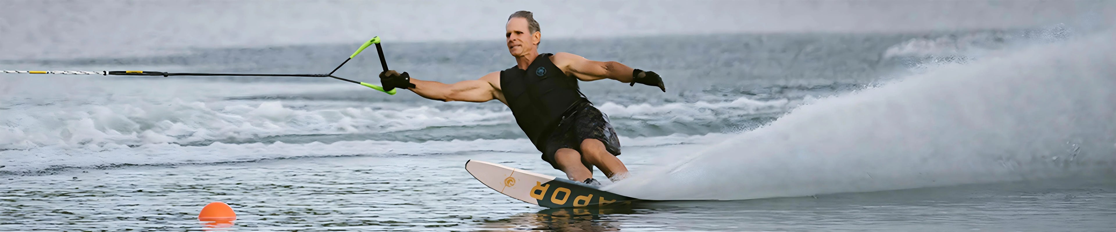 Man water skiing on lake with wakeboard, splashing water, wearing black vest, at Welcome Boardstore