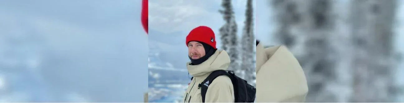 Man in red beanie, snow jacket, and backpack outdoors in snowy mountain setting