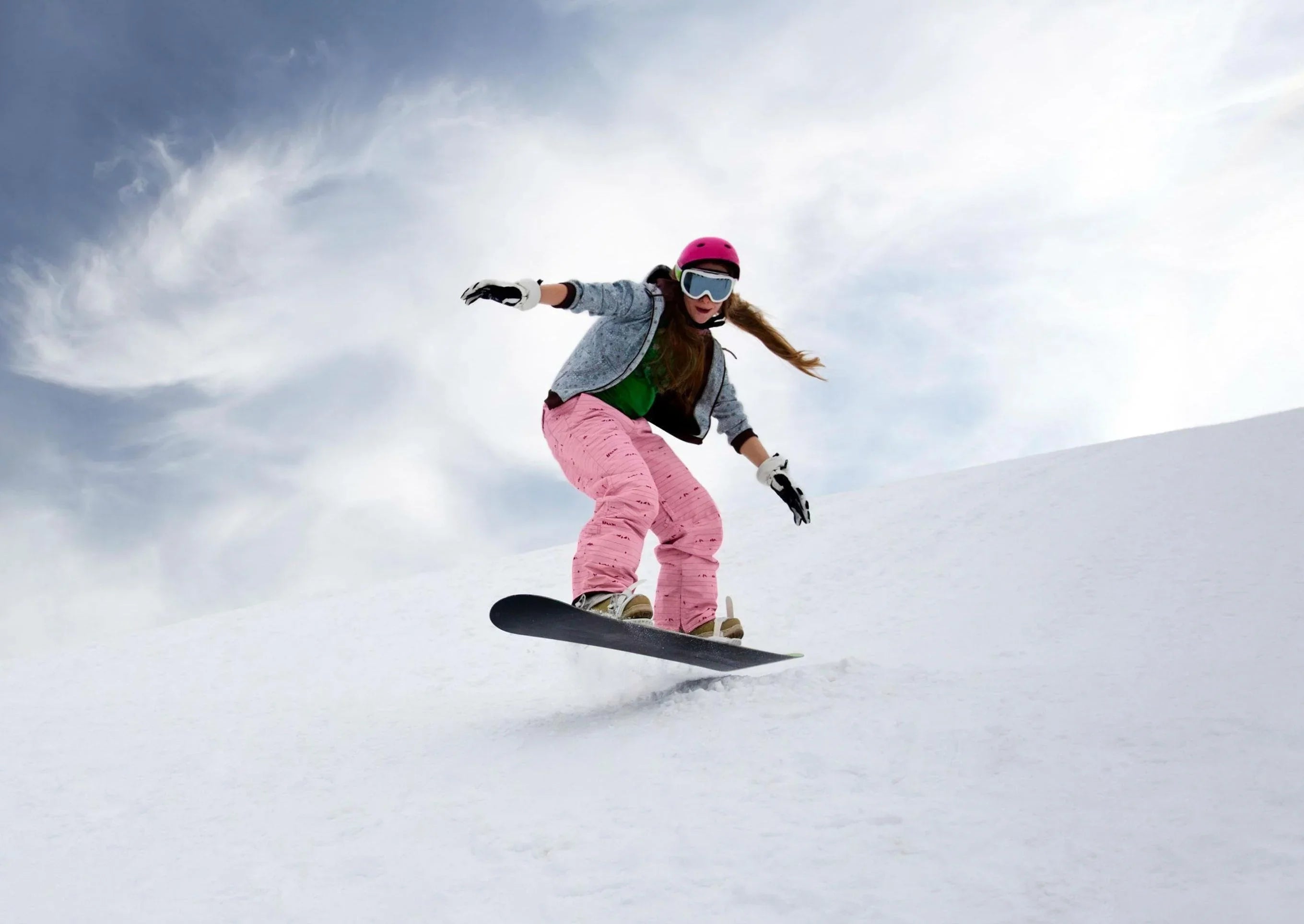 Woman snowboarding on snowy slope in winter gear, showcasing snowboarding essentials