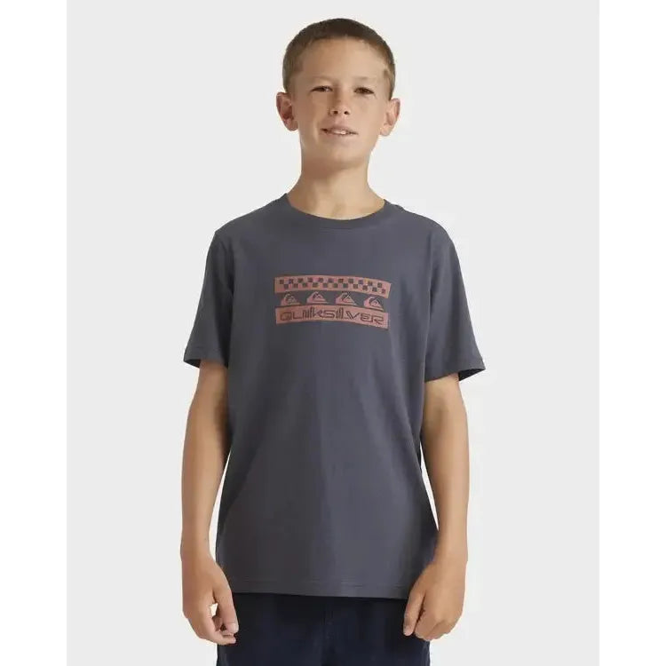 Boy wearing a dark grey Quiksilver graphic t-shirt and navy shorts, standing against light background