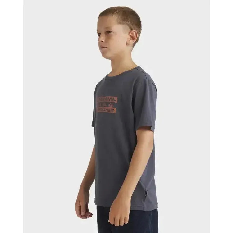 Boy wearing a dark grey surf graphic t-shirt and dark shorts, side view