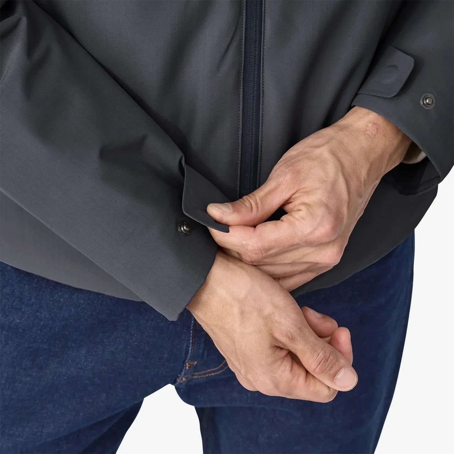 Person adjusting the cuffs of a dark gray jacket on a white background
