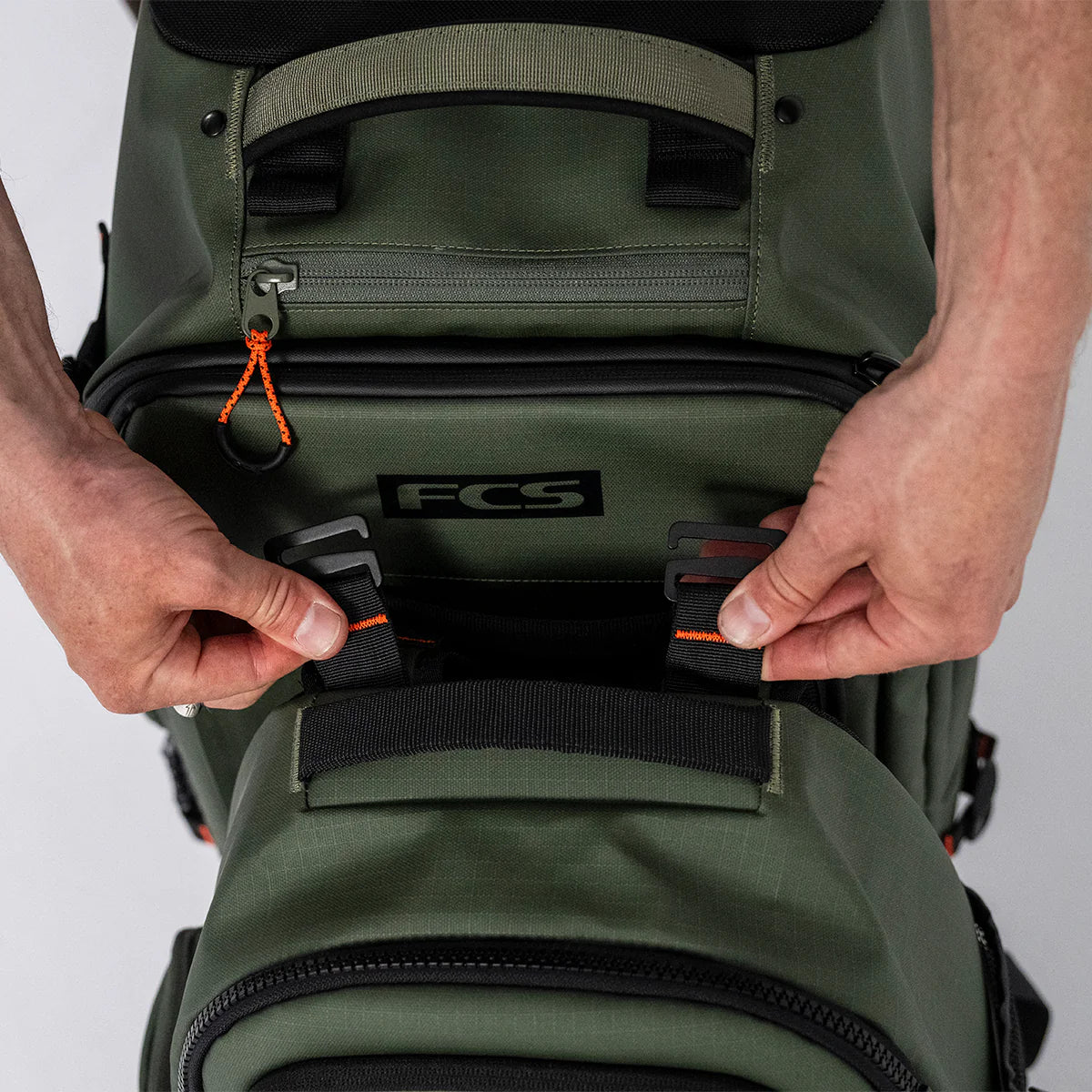 Person adjusting a FCS Day X Pack 24L green backpack with visible branding on a white background