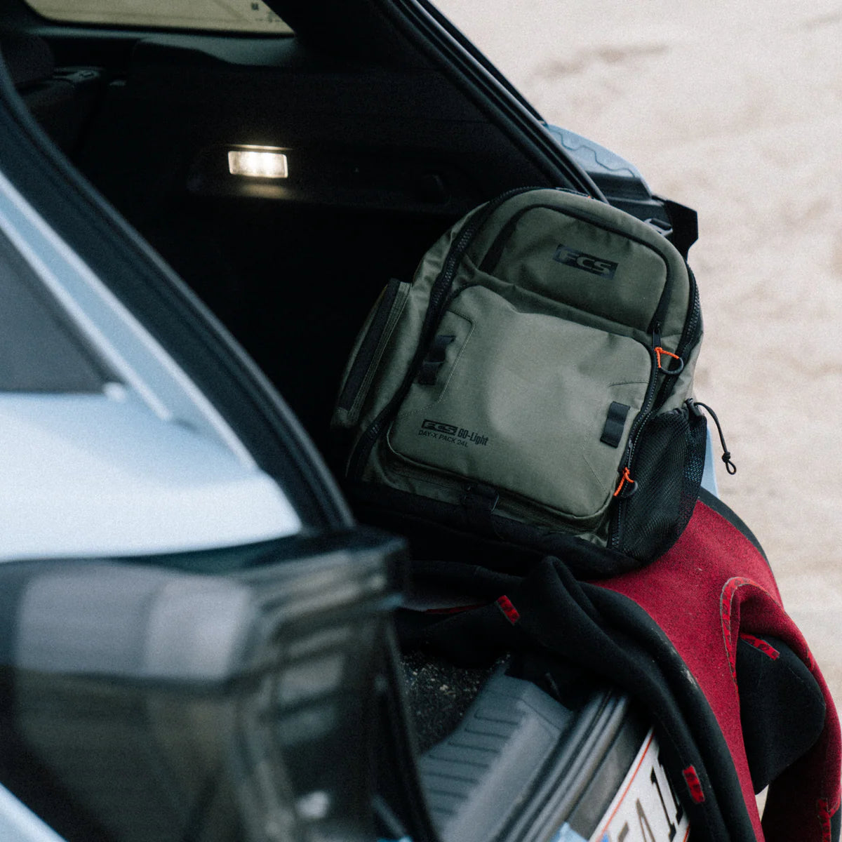 Green FCS Day X Pack 24L backpack on a person's lap next to an open car door
