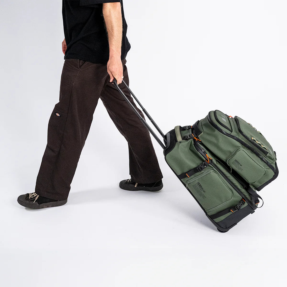 Person pulling a green FCS Day X Pack 24L and suitcase on a white background
