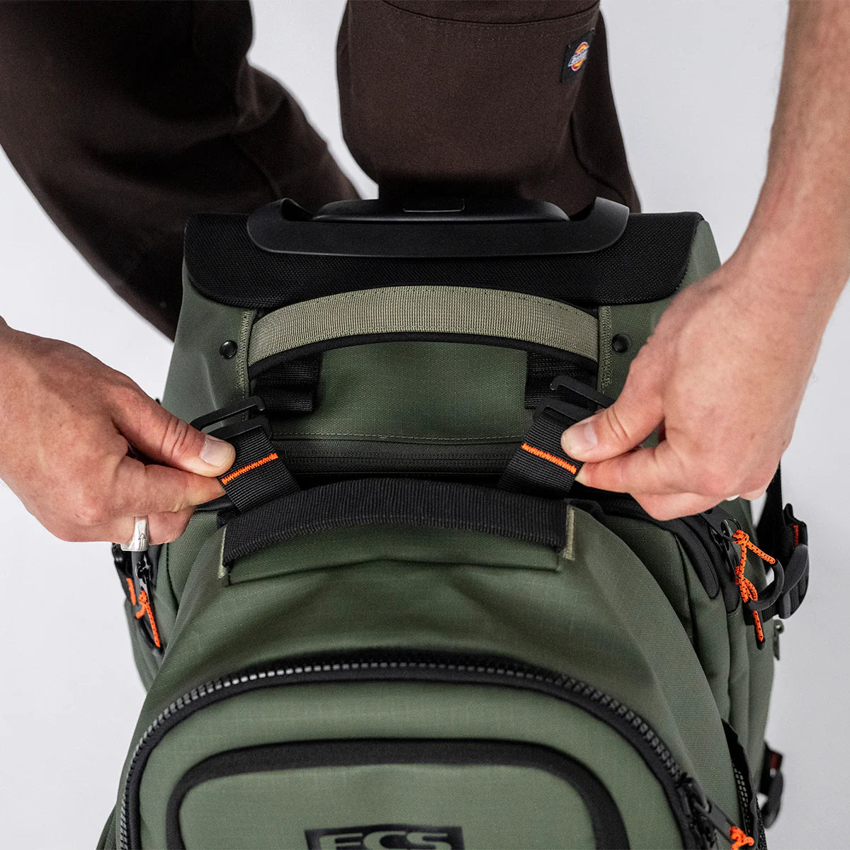 Person adjusting a green FCS Day X Pack 24L backpack with visible branding on a plain background