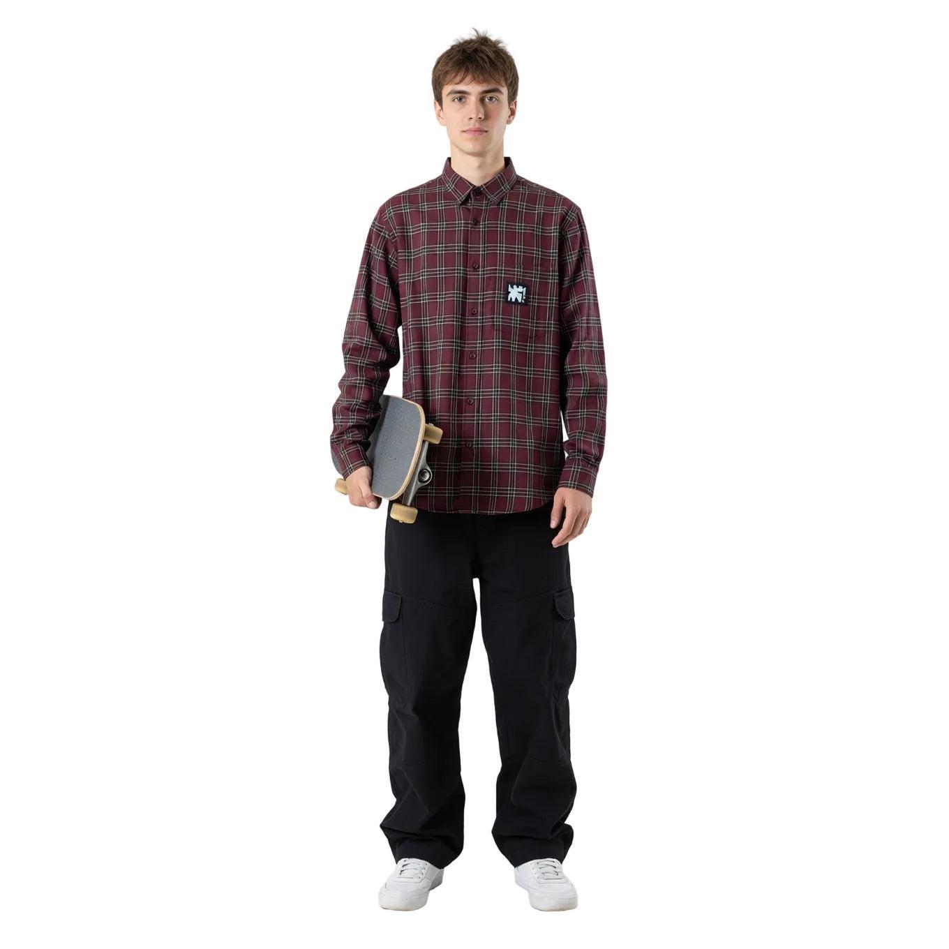 Person wearing a plaid shirt with a logo, holding a skateboard, on a white background welcome boardstore