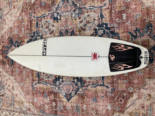 White Pyzel Red Tiger pre-loved surfboard deck with black flame tail pad on a patterned rug Welcome Board Store