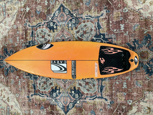 Orange Sharpeye HT2 Youth pre-loved surfboard deck with black flame tail pad on a patterned rug Welcome Board Store