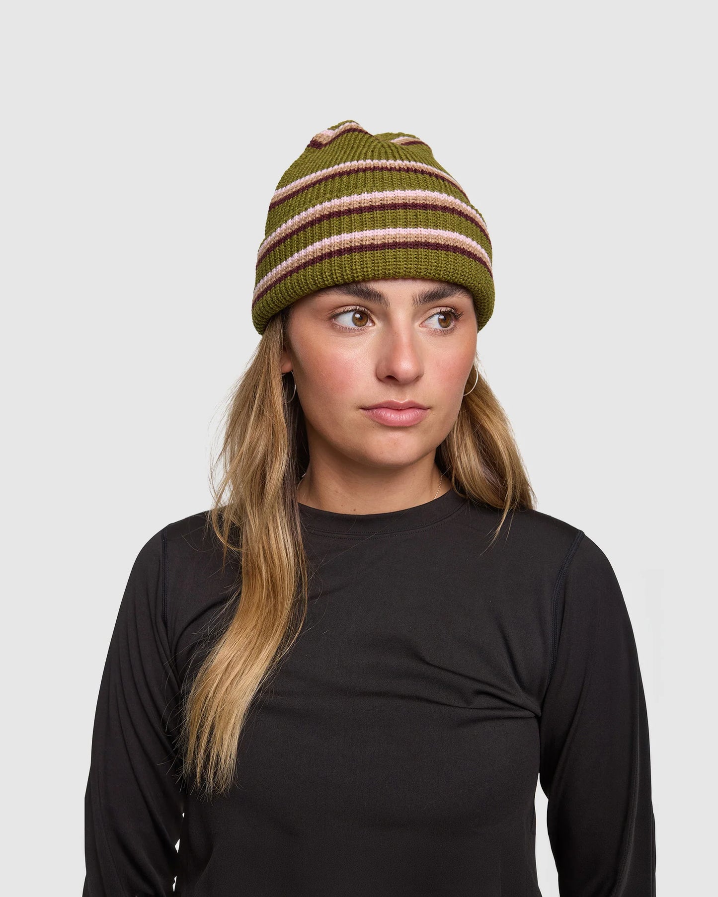 Woman wearing a green and pink striped beanie against a plain background