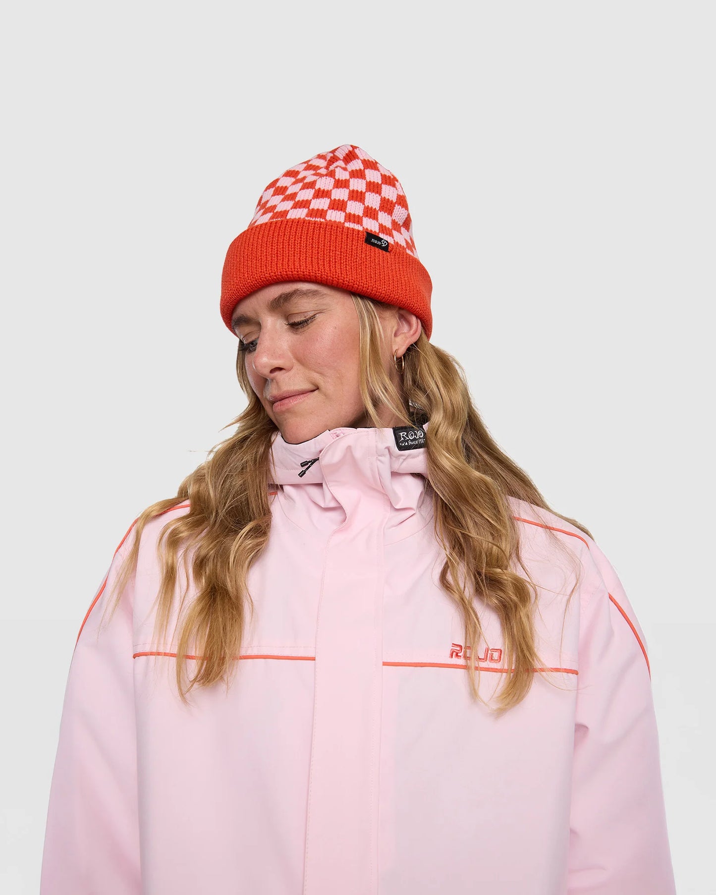 Rojo Cosy Check Beanie Person wearing a pink jacket and red checkered beanie on a white background