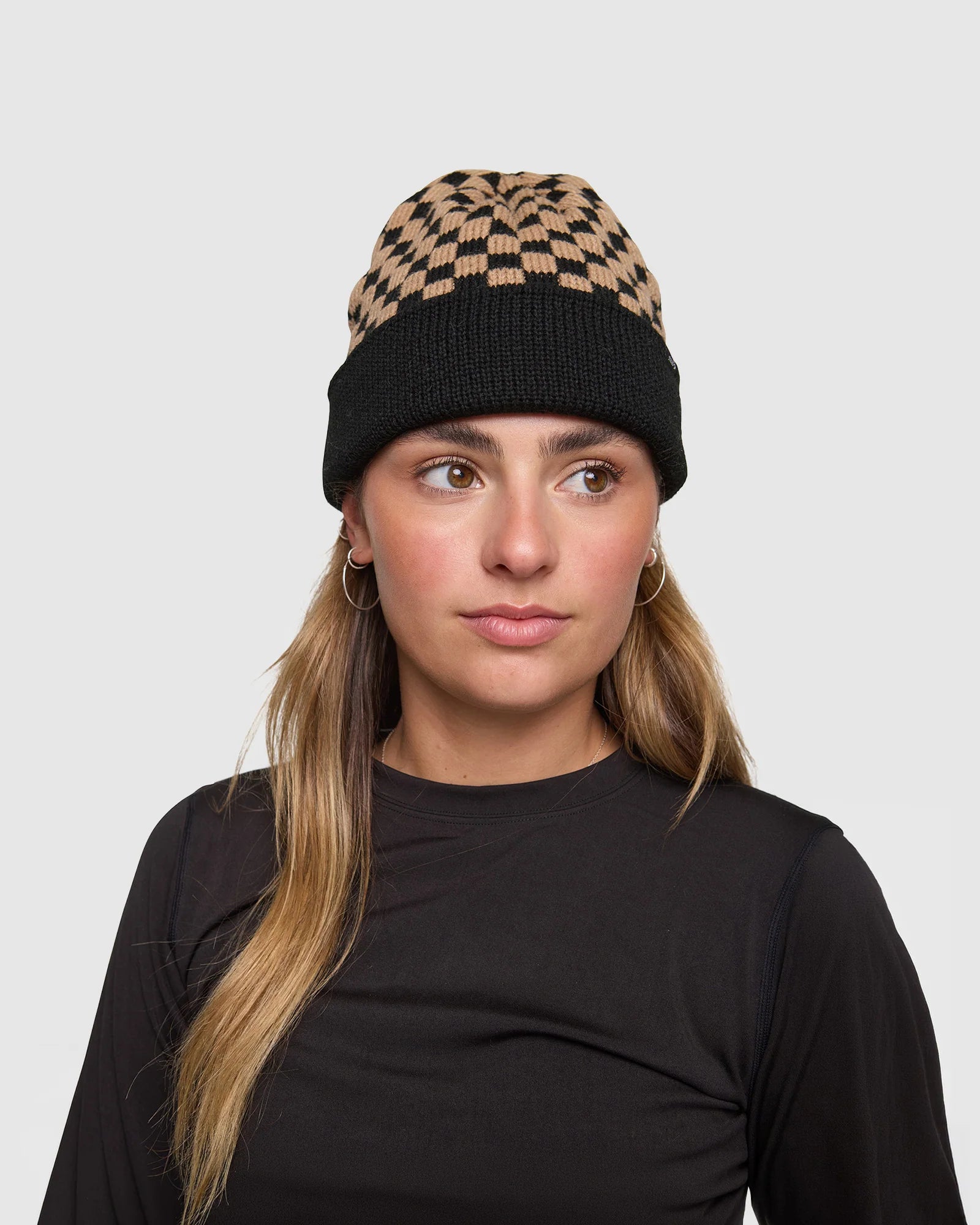 Woman wearing a black and beige checkered beanie on a light gray background