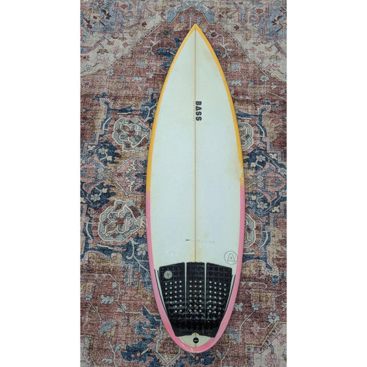 Surfboard with 'BASS' branding on a patterned rug
