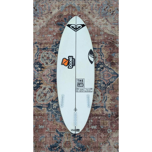 White surfboard with branding on a patterned rug