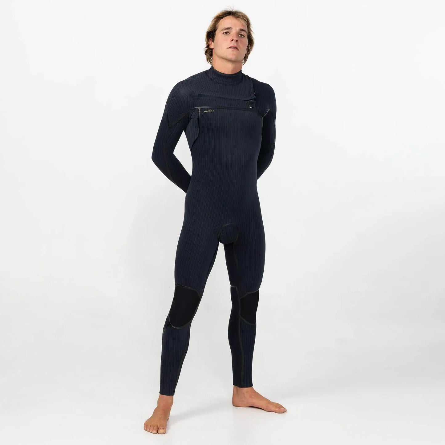 Man wearing a black full-length chest zip wetsuit, standing barefoot on white background