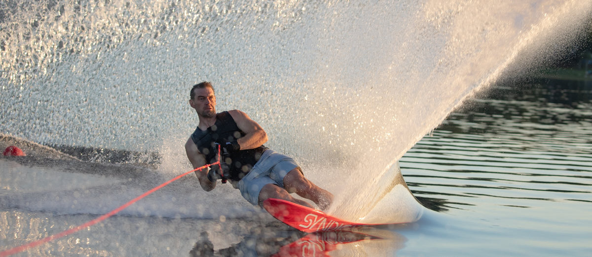 Slalom skier on an HO Syndicate ski throwing golden spray at sunset